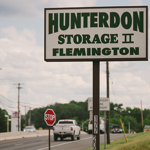 a sign on the end of a tall pole with the words Hunterdon Storage II Flemington in green text on the white sign